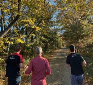Three men running on a trail with fall foliage