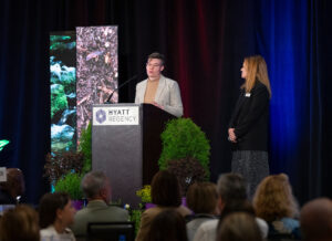 A woman standing behind a podium surrounded by greenery