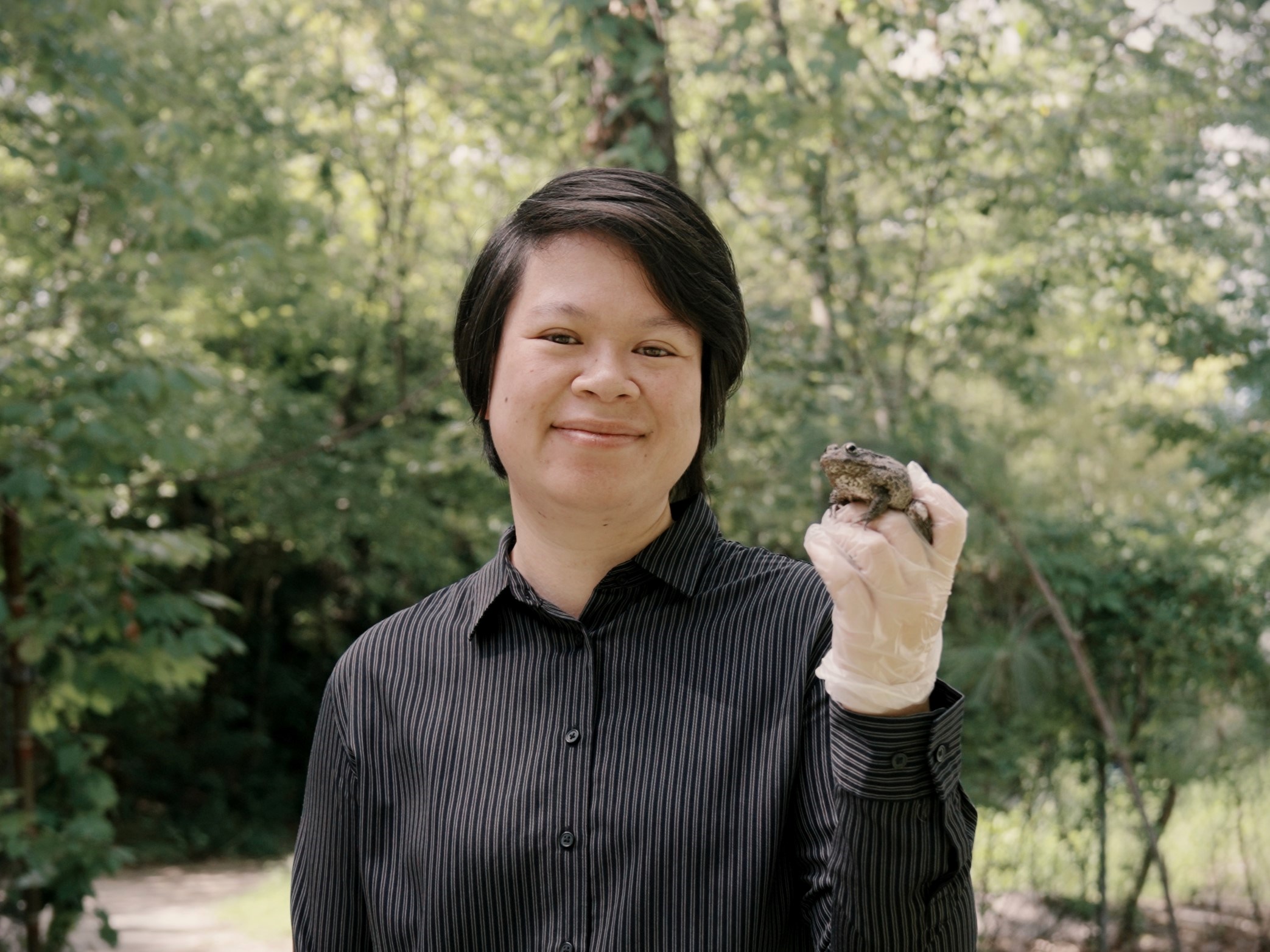 Sheila Poo headshot: A woman with dark hair and a black shirt holds a frog