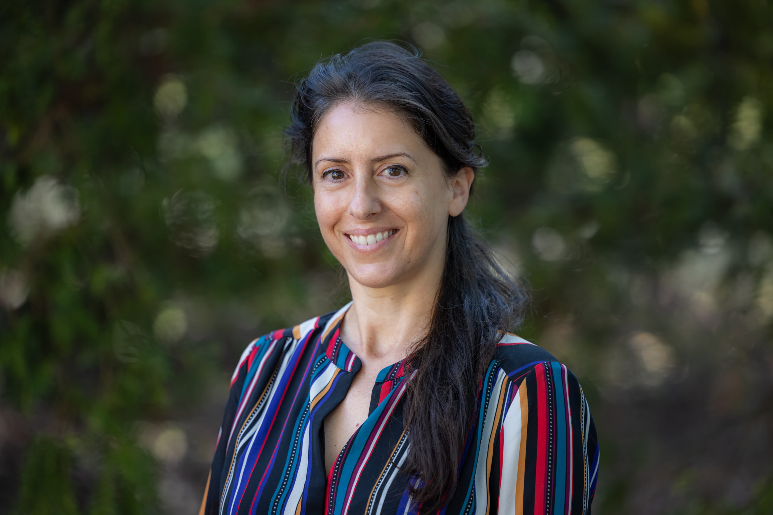 Malu Celli headshot: A woman with long dark hair in a striped shirt, smiling