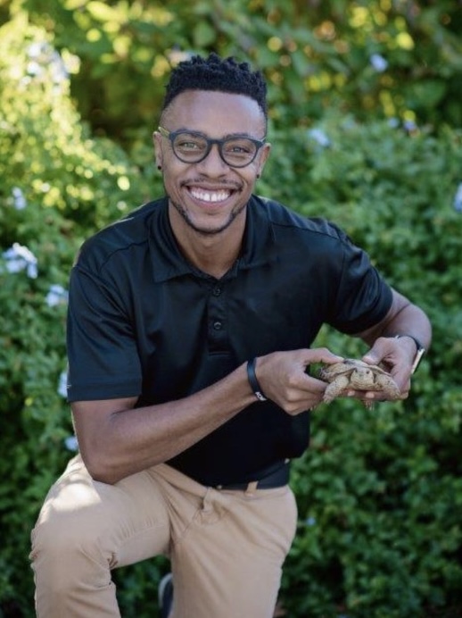 Chris Conner headshot: A man with glasses in a black shirt smiles, holding a snake